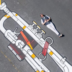 A man lying in the street parallel to drawn street art of a trumpet