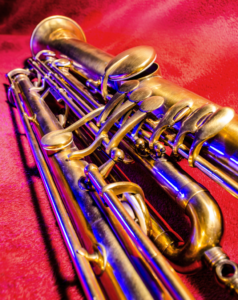 An artistic photo of a brass sarrusophone on a red velvet background with blue light shining down on it.