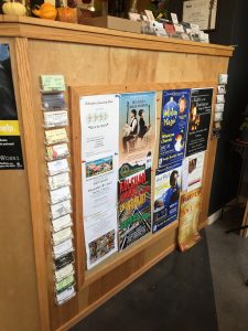 A bulletin board with several posters on it, framed by two racks of  business cards