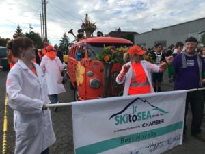 Several people in white lab coats and orange safety gear march behind a banner that reads: 