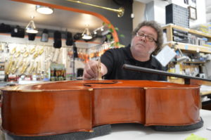 A man holds a cello bridge upright on the top side of a cello that is laying on its back without strings.