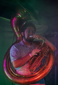 Maxwell plays a sousaphone in a colorful atmosphere